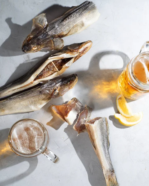 Dry salted fish and mugs with light beer on a light table. Snack for beer and beer. Beer party and snacks for a group of friends