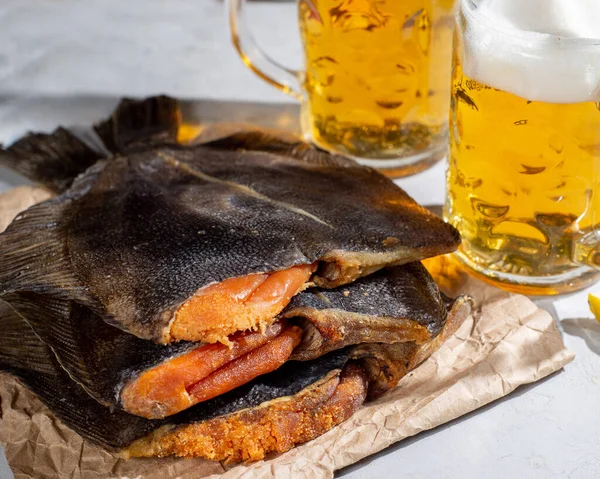 Dry salted fish and mugs with light beer on a light table. Snack for beer and beer. Beer party and snacks for a group of friends