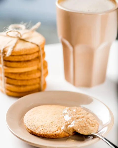 Cookies are smeared with peanut butter. Cup of tea or coffee on background
