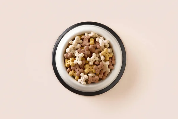 Dry dog food in bowl on beige background. Healthy nutrition in bone shape for pets