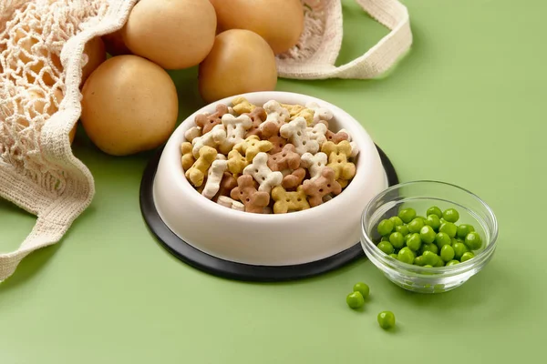 Dry dog vegan vegetarian food concept. Raw vegetables and green near bowl with pet feed on green background