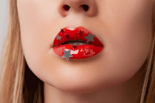 Close up macro womans plump lips with red gloss and silver stars. Beauty fashion portrait personal make up. Beauty salon concept