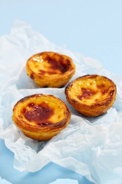 Geleneksel Portekiz yumurtalı tart tatlısı Pasteis Pastel de nata veya Pasteis de Belem mavi arka planda. Yerel hamur işi kafeteryası kavramı