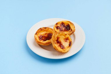 Geleneksel Portekiz yumurtalı tart tatlısı Pasteis Pastel de nata veya Pastels de Belem mavi arka planda tabakta. Yerel hamur işi kafeteryası kavramı