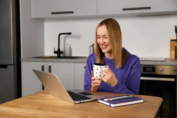 Happy young adult woman work study at kitchen using laptop. Remote education. Work from home concept
