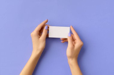 Womans hands holding business card on purple background. Business work template mockup. Empty greeting card with space for text