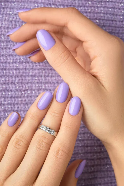 Manicured womans hands on violet knitted fabric. Manicure, pedicure beauty salon concept. Empty place for text