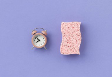 Pink sponge with alarm clock on purple background. Cleaning service or housekeeping creative layout