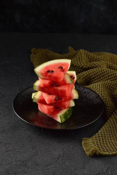Watermelon on black background. Sliced fruit on the plate. Summer refreshing dessert