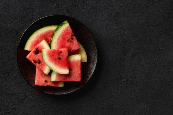 Flat lay top view watermelon on black background. Sliced fruit on the plate. Summer refreshing dessert