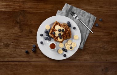 Kırsal ahşap masada muzlu ve yaban mersinli Belçika waffle 'ı. Sağlıklı kahvaltı diyeti tarifi düz bir görünüm yatıyordu