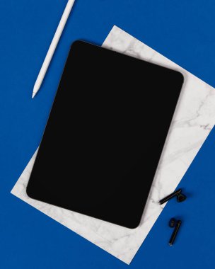Düz görünüm mavi zemin üzerinde boş ekran dijital tablet yatıyordu. Merkez ofis çalışma alanı. İş çalışma şablonu.