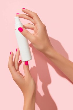 Kadınların elleri pastel pembe arka planda beyaz şişe tutuyor. Kişisel bakım güzellik tedavisi konsepti. Cilt rutini