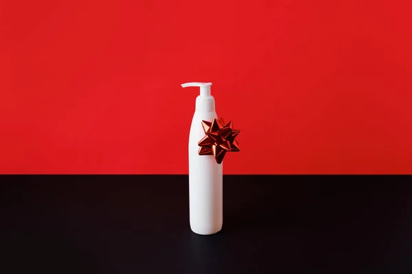White bottle of cosmetics cream or cleansing foam with bow on red-black background. Halloween black friday sale concept with copy space