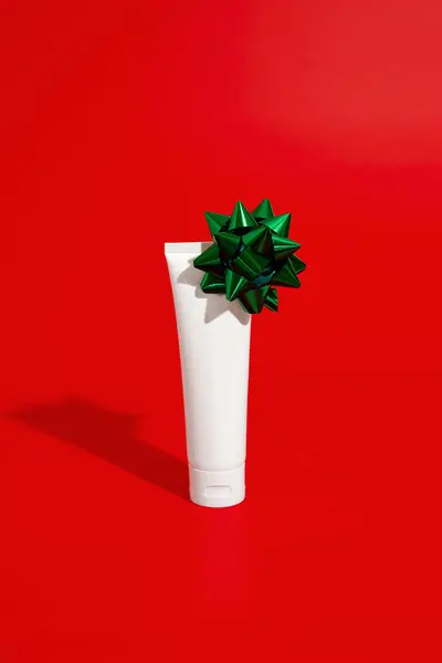 Blank white cosmetic plastic tube on red background with bow. Christmas Valentines day sale concept. Mock up template in minimal style