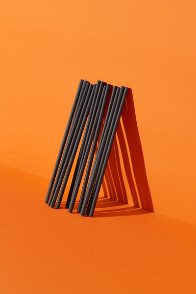 Black paper straws on orange background. Halloween party. Drinks and food concept
