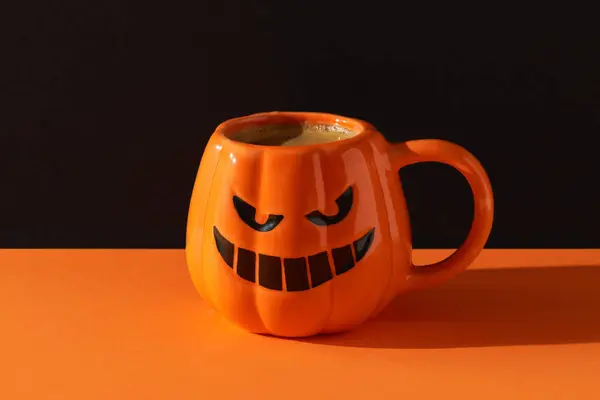 Cappuccino latte coffee in pumpkin cup on black orange background. Halloween celebration concept. Menu for restaurant