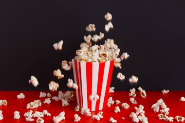 Kırmızı ve siyah arka planda patlamış mısırlı çizgili kutu. Sinema, sinema ve eğlence konsepti.