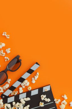Patlamış mısır, 3 boyutlu gözlük ve turuncu arka planda el çırpma tahtası. Düz konum, kopyalama alanı. Sinema, sinema ve eğlence konsepti.