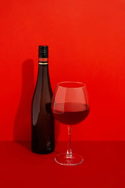 Bottle and glass of wine. Alcoholic drink on red background with deep shadows. Mock up drink with place for you logo and text.