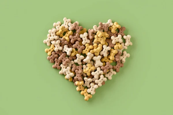 Dry dog food in heart shape on green background. Healthy organic nutrition in bone shape for pets
