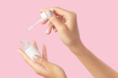 Kadınların elleri pastel pembe arka planda damlatıcıyı tutuyor. Kişisel bakım güzellik tedavisi konsepti. Sabah cildi rutini