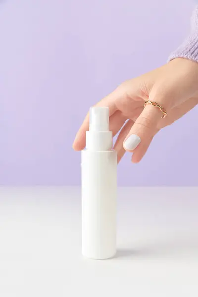 在紫丁香背景上 女人用手触摸白色的瓶子管 自理美容疗法的概念 护肤产品洗浴配件 图库照片