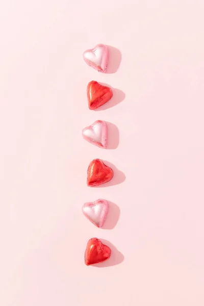 粉红背景的心形巧克力糖果的垂直线条 情人节的概念 平躺在床上 免版税图库图片