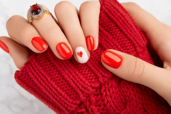 Manicured womans hands in warm wool red sweater. Fashionable valentines day nail design. Trendy fashion accessories