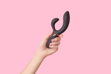 Pembe ojeli kadın eli pembe arka planda siyah bir vibratör tutuyor. Yetişkinler için seks oyuncakları
