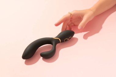 Pembe ojeli kadın eli, şeftali pembesi arka planda duran siyah vibratöre dokunuyor. Yetişkinler için seks oyuncakları