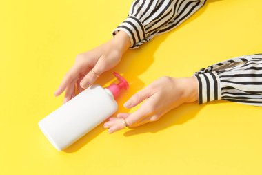 Sarı arka planda beyaz şişeyi tutan kadınların elleri. Kişisel bakım güzellik tedavi kavramı.