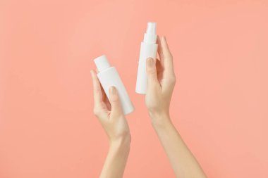 A womans hands holding a white cosmetic bottles on a peach background. Care products beauty treatment concept