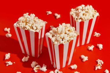 Kırmızı arka planda patlamış mısırlı çizgili kutular. Sinema, sinema ve eğlence konsepti.