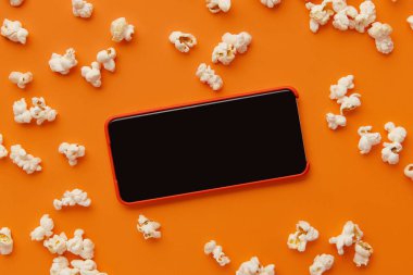 Turuncu arka planda akıllı telefon ve patlamış mısır. Sinema, sinema ve eğlence konsepti.