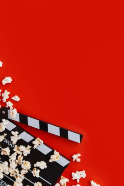 Kırmızı arka planda patlamış mısır ve el çırpma tahtası. Düz konum, kopyalama alanı. Sinema, sinema ve eğlence konsepti.