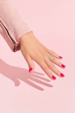 Pembe tırnak tasarımlı kadın eli. Manikür, pedikür güzellik salonu konsepti. Moda rengi. Mesaj için boş bir yer. Derin uzun gölgeler.