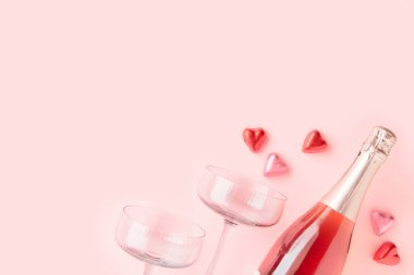 Pembe arka planda iki bardak ve kalp şeklinde çikolata şekerlemeli bir şişe köpüklü şarap ve fotokopi alanı. Sevgililer Günü konsepti. Düz yatıyordu