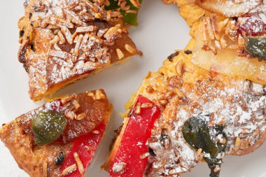 Kesilmiş bir bayram pastasının ayrıntılı bir görüntüsü. Üstünde şeker, kiraz, badem ve pudra şekeri var.