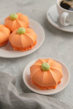 Arkaplanda daha fazla tatlı ve kahve olan bir tabakta tek bir balkabağı şeklinde tatlı.