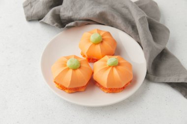 Kabak şekilli tatlılar, tabakta yeşil tepsiler, katlanmış gri bir peçetenin yanına yerleştirilmiş.