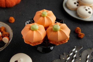 Siyah bir standın üzerinde yeşil tepeli üç tane balkabağı şekilli tatlı yakın plan