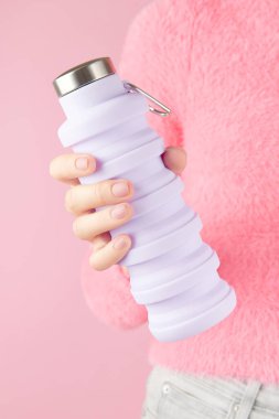 Pembe arka planda yeniden kullanılabilir leylak suyu şişesi tutan kadın. Sıfır atık, sürdürülebilir yaşam tarzı