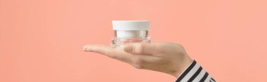 A womans hand holds a tube of cream on a peach background. Self care beauty treatment concept
