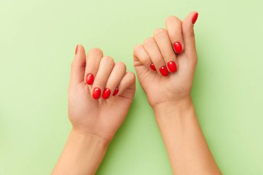 Yeşil arka planda kırmızı manikürlü kadın elleri. Minimalist tırnak tasarımı. Güzellik salonu konsepti
