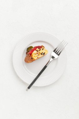 Bir dilim meyveli pasta ve yanında çatal olan beyaz bir tabakta fındık.