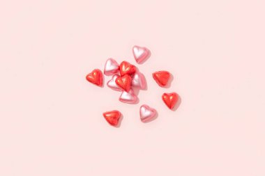 Wrapped heart-shaped chocolates in red foil on a pink background with deep shadows. Valentines Day concept