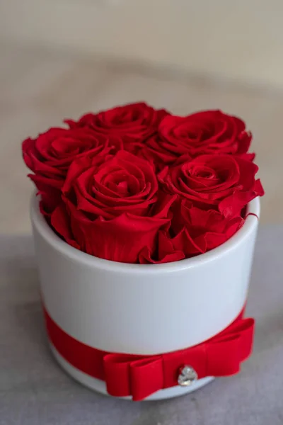Top view of red long-lasting preserved roses in a white acrylic flower box with a red bow. Romantic present.