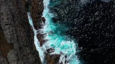 Derin mavi sulardan inen dronun yukarıdan aşağı görüntüsü. Güçlü dalgalar Fuerteventura adasındaki siyah volkanik kayalara çarpıyor ve köpürüyor. Seyahat ve tatil kavramı.