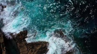Derin mavi suyun üzerinde uçan İHA 'nın yukarıdan aşağı görüntüsü. Güçlü dalgalar Fuerteventura adasındaki siyah volkanik kayalara çarpıyor ve köpürüyor. Seyahat ve tatil kavramı.